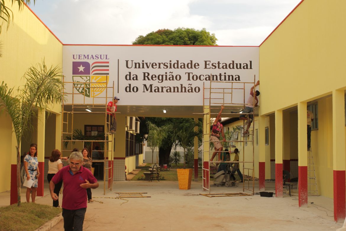 Fachada da universidade com pessoas trabalhando para colocação do painel.