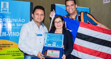 Orientador Zilmar Timóteo e orientando comemoram premiação. Reitora Elizabeth Nunes Freire e orientador seguram premiações. Orientando, Brunno Gustavo segura bandeira do Maranhão representando os discentes do curso.