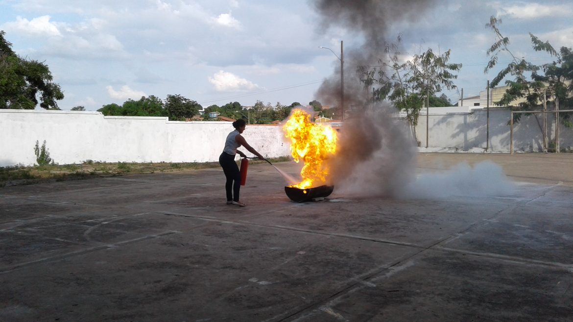 Uma mulher apaga o incêndio provocado no interior de um tanque de simulação com auxílio de um extintor.