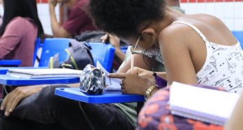 Aluna dentro da sala de aula escrevendo em seu caderno.