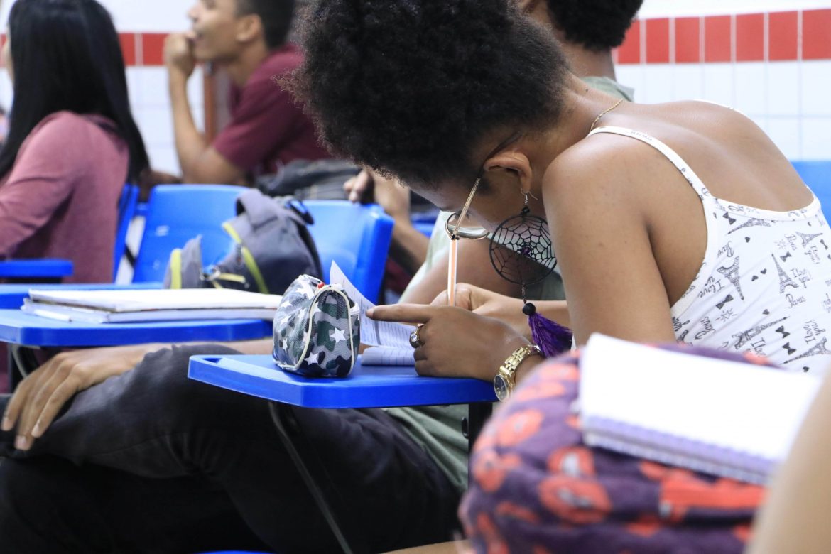 Aluna dentro da sala de aula escrevendo em seu caderno.