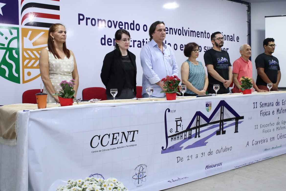 Mesa do auditório com a presença de reitoria, pró-reitoria, professores e representante acadêmico.