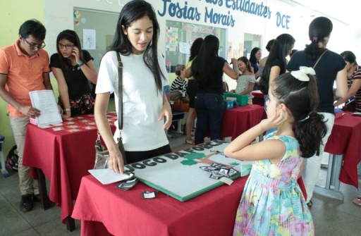 Acadêmica do curso de Pedagogia com uma criança perto de um jogo que se encontra em uma mesa.