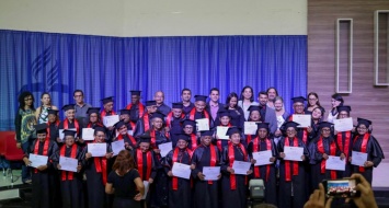 Turma de formandos da UATI reunidos no palco e apresentando seus diplomas de conclusão graduação.