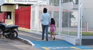 Uma mulher adulta caminha pela calçada tátil da UEMASUL de mãos dadas com uma criança.