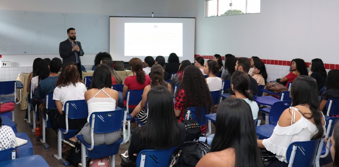 Homem em pé ministrando uma palestra para alunos sentados em uma sala de aula 