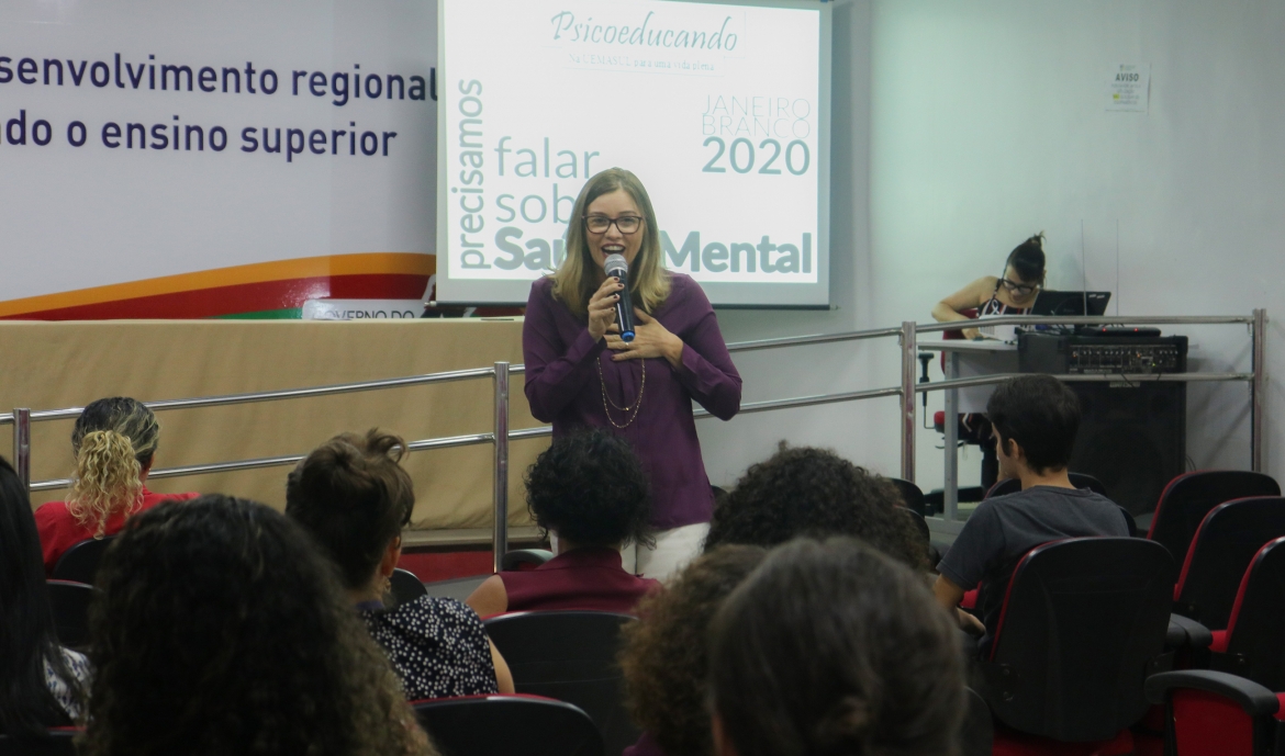 Palestrante em pé de frente para a plateia. Todos estão de costas observando a palestrante.