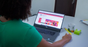 A foto mostra uma moça de blusa verde, de costas, navegando no site da UEMASUL em um notebook.