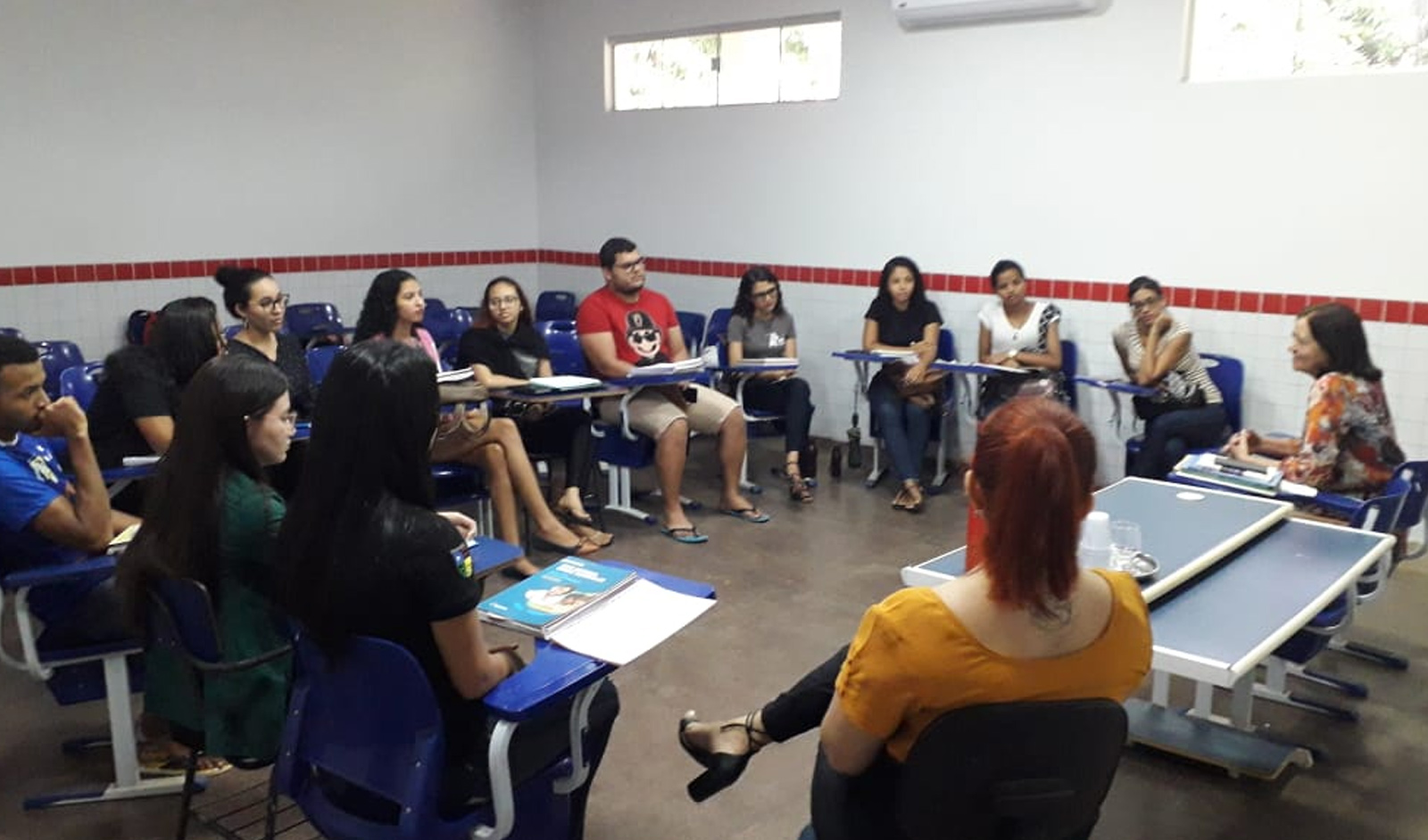 Grupo de pessoas em sala de aula, sentadas em círculo. 