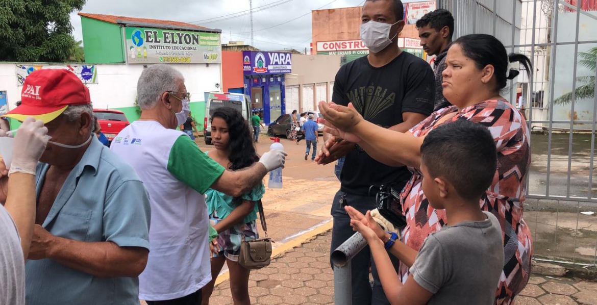 Pessoas na rua, com máscaras usam álcool gel nas mãos.